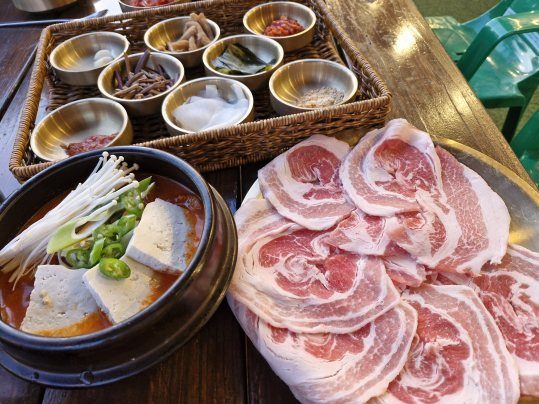얇게 썬 생삼겹살과 두부·팽이버섯 뚝배기 찌개, 놋그릇 반찬