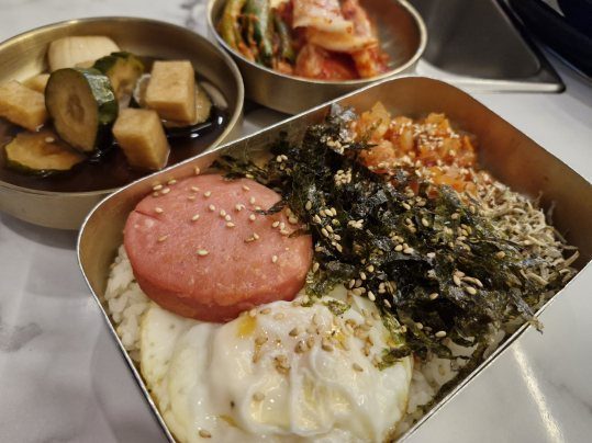 밥 위에 햄·달걀프라이·김가루·김치·멸치볶음을 올린 도시락과 장아찌