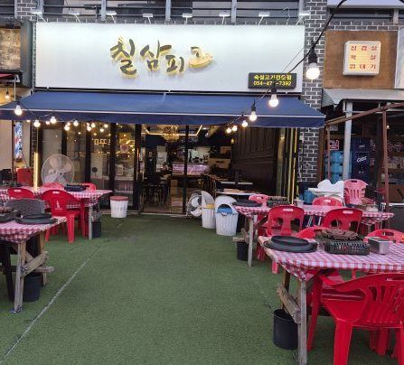 줄 전구 아래 빨간 체크 식탁보 테이블이 놓인 가게 앞 마당