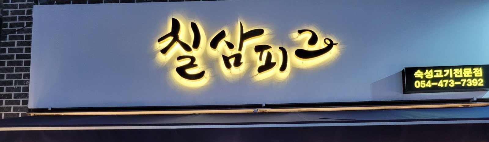 밤에 불이 켜진 간판 «칠삼피그»와 «숙성고기전문점 054-473-7392» 전광판